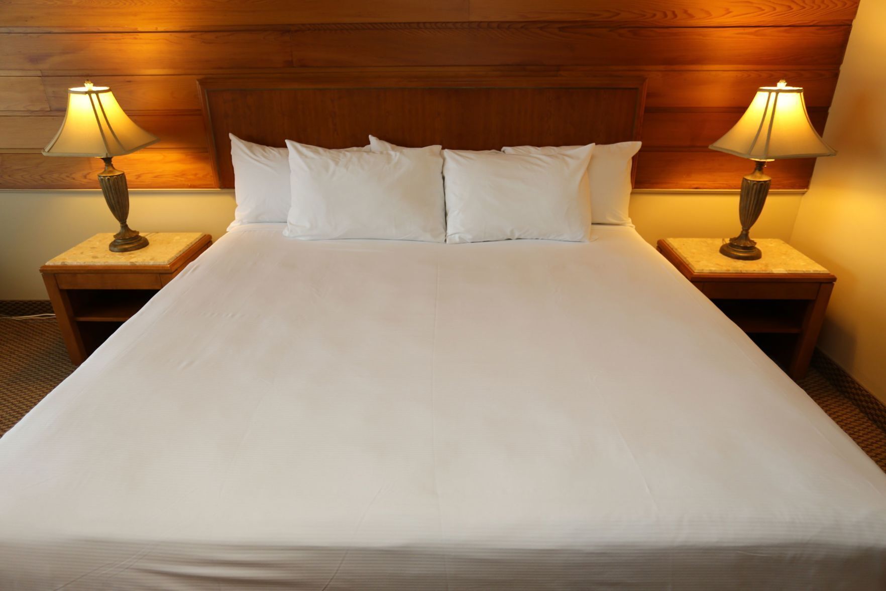 A hotel room with a large bed, two bedside lamps, and a wooden headboard.