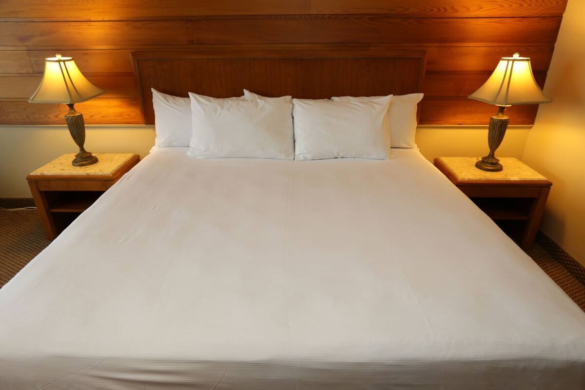 A hotel room with a large bed, two bedside lamps, and a wooden headboard.