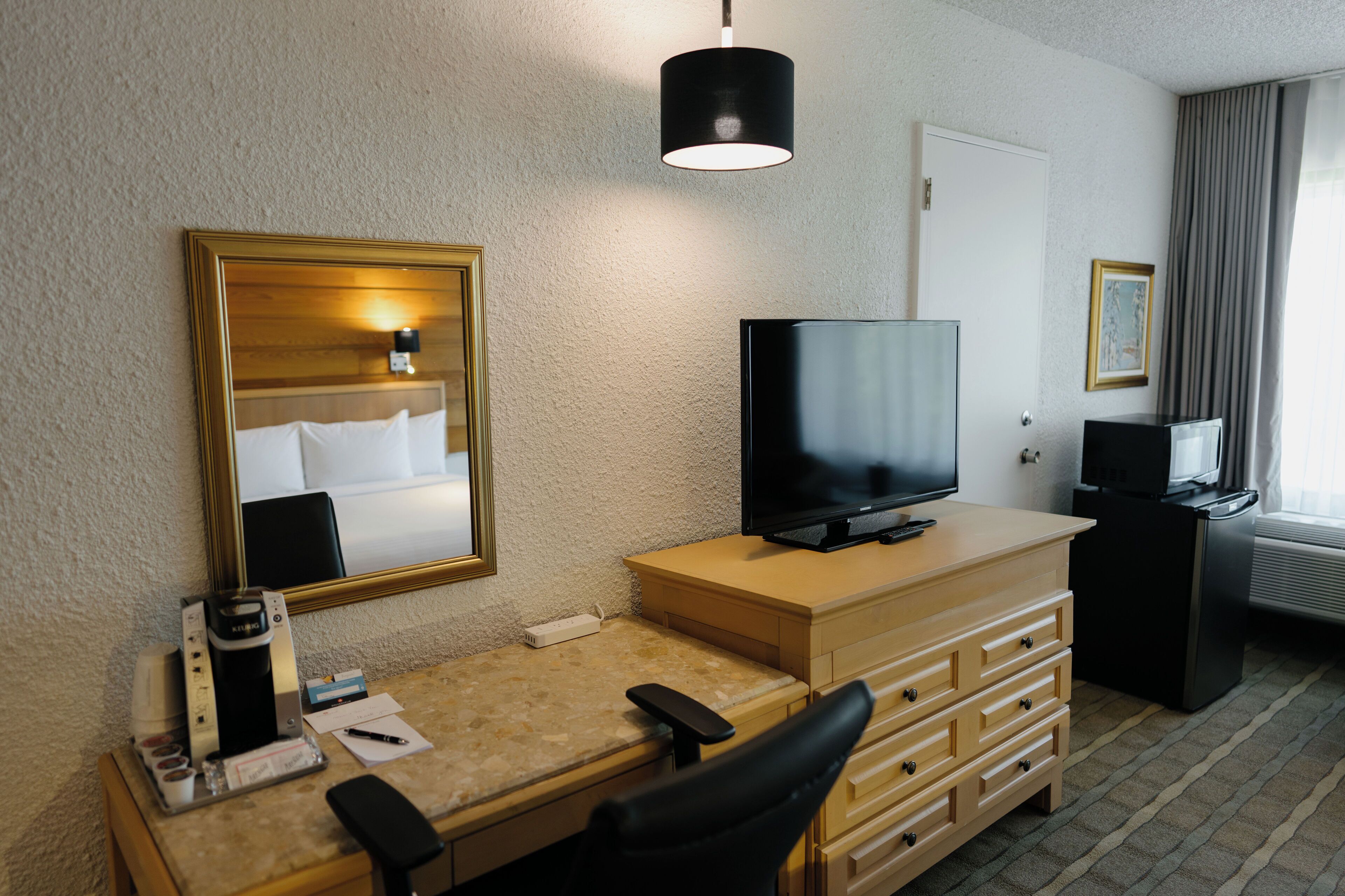 Habitación de hotel con escritorio, silla, televisor y espejo.