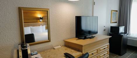 Habitación de hotel con escritorio, silla, televisor y espejo.