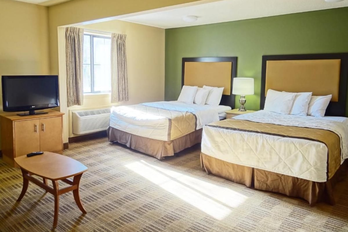 A hotel room with two beds, a television, a small table, and a window with curtains.