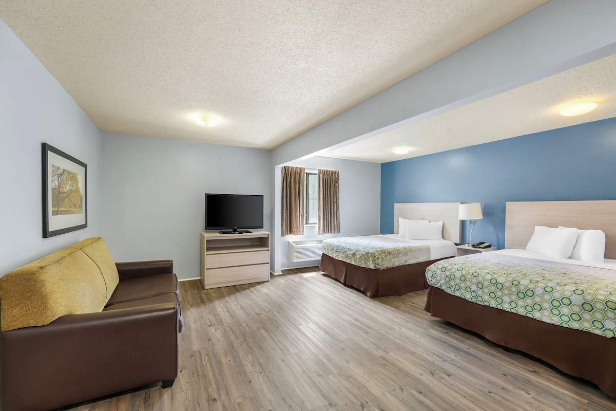 A hotel room with a sofa, a TV, two beds, a desk, and a window with curtains.