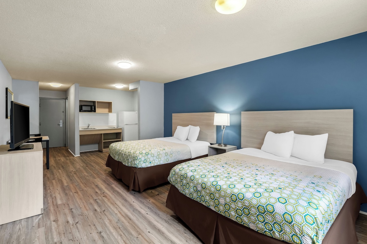 A hotel room with two beds, a desk, a microwave, and a television.