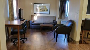 Un salon comprenant un canapé, une table basse, un téléviseur et un bureau avec une chaise.