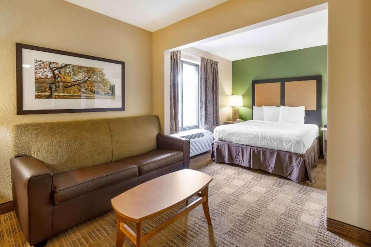 A hotel room with a bed, a sofa, a table, and a framed picture on the wall.