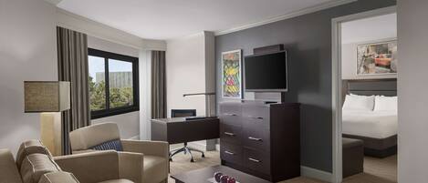 A hotel room with a sofa, a desk, a dresser, a TV, and a bed.