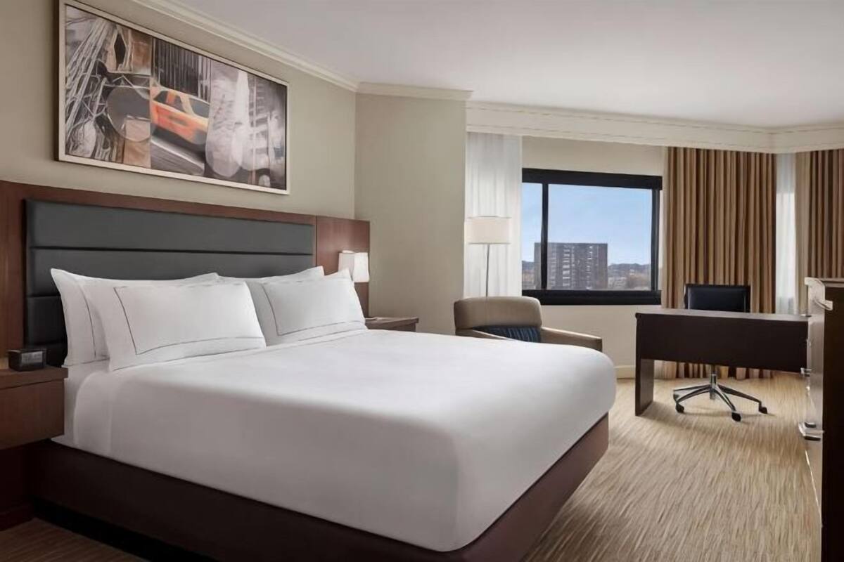 A hotel room with a large bed, a desk, a chair, and a city view.