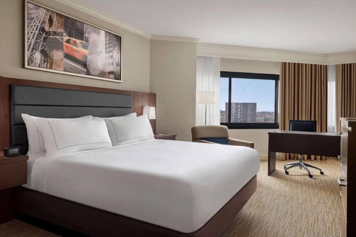 A hotel room with a large bed, a desk, a chair, and a view of the city.