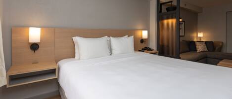 Una camera d'albergo moderna con un letto grande, due lampade da comodino, una testiera in legno, un comodino e un'area salotto con divano e cuscini.