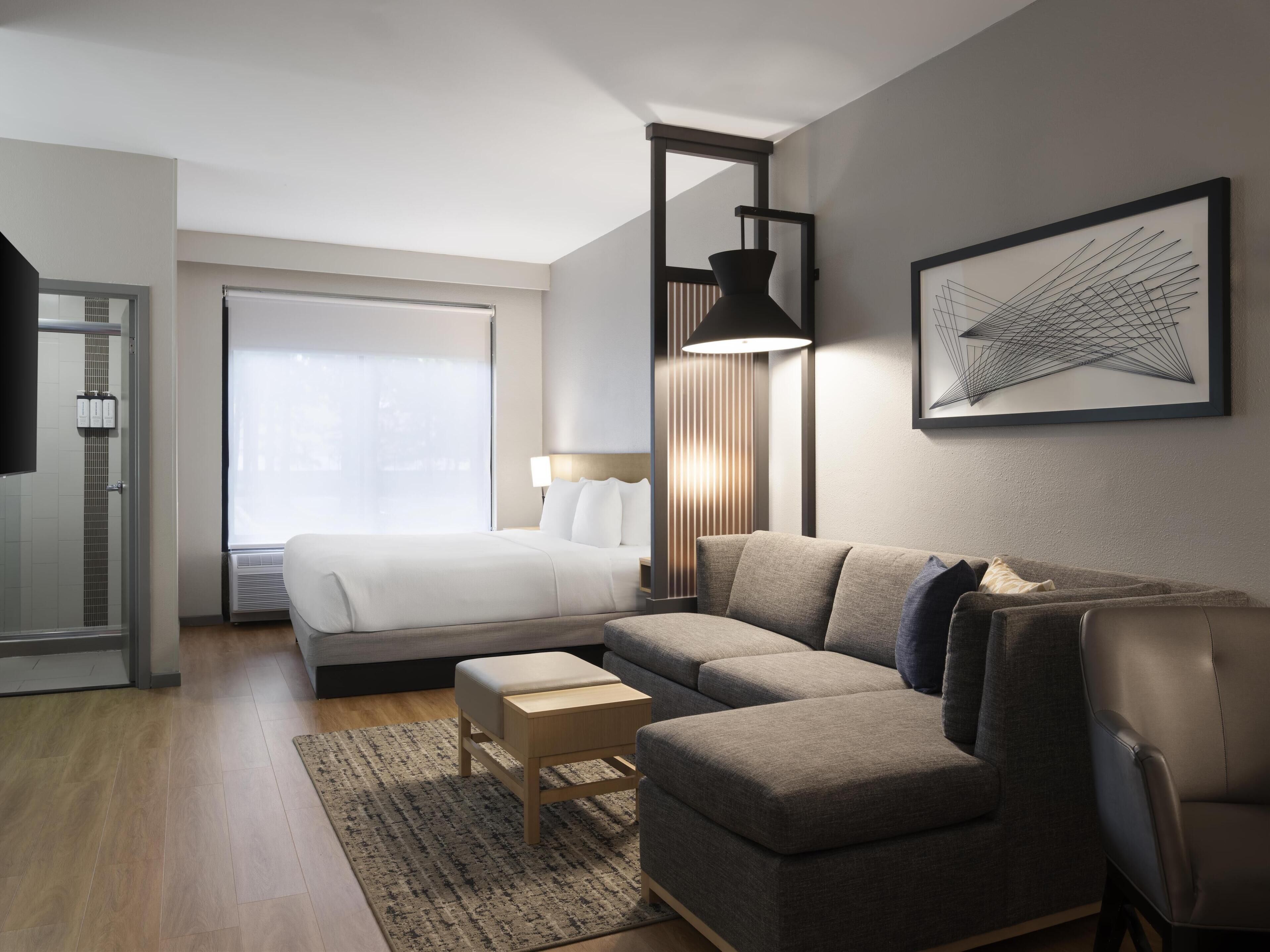 Una habitación de hotel moderna con cama, sofá, escritorio y una ventana grande.