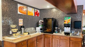 Une cuisine avec un mur recouvert de carreaux, des meubles en bois, un four à micro-ondes, une machine à café et un distributeur de jus.