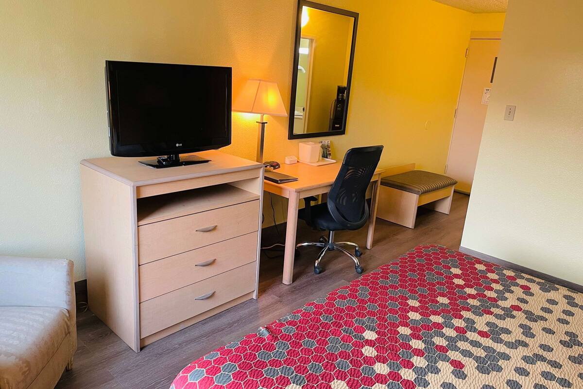 Une chambre d’hôtel équipée d’un bureau, d’une chaise, d’une télévision, d’une lampe et d’un lit agrémenté d’un tapis à motifs.