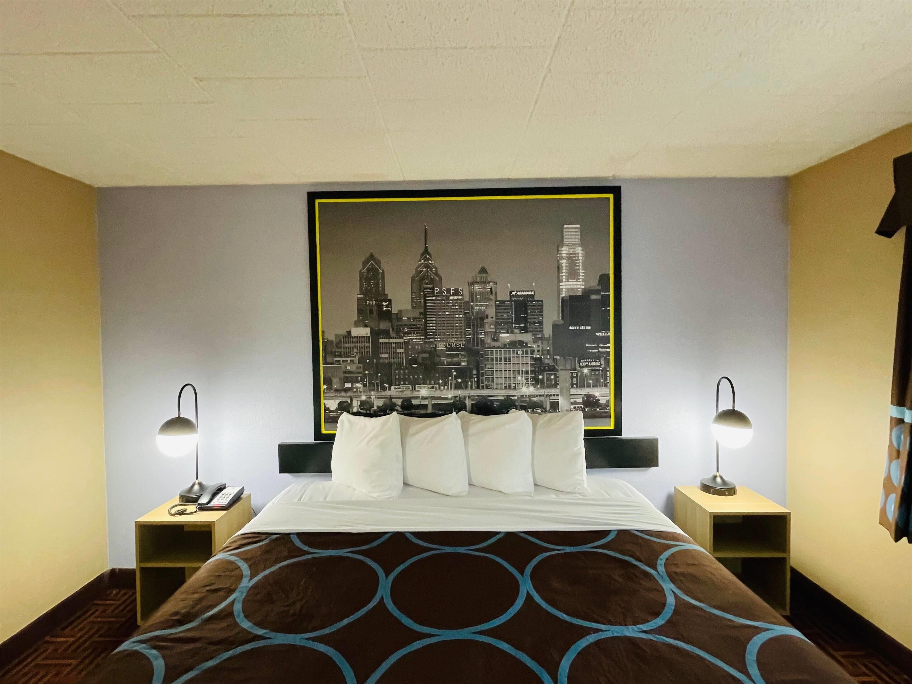 Una camera d'albergo con un letto, due comodini, un quadro con una veduta cittadina e una coperta a motivi.