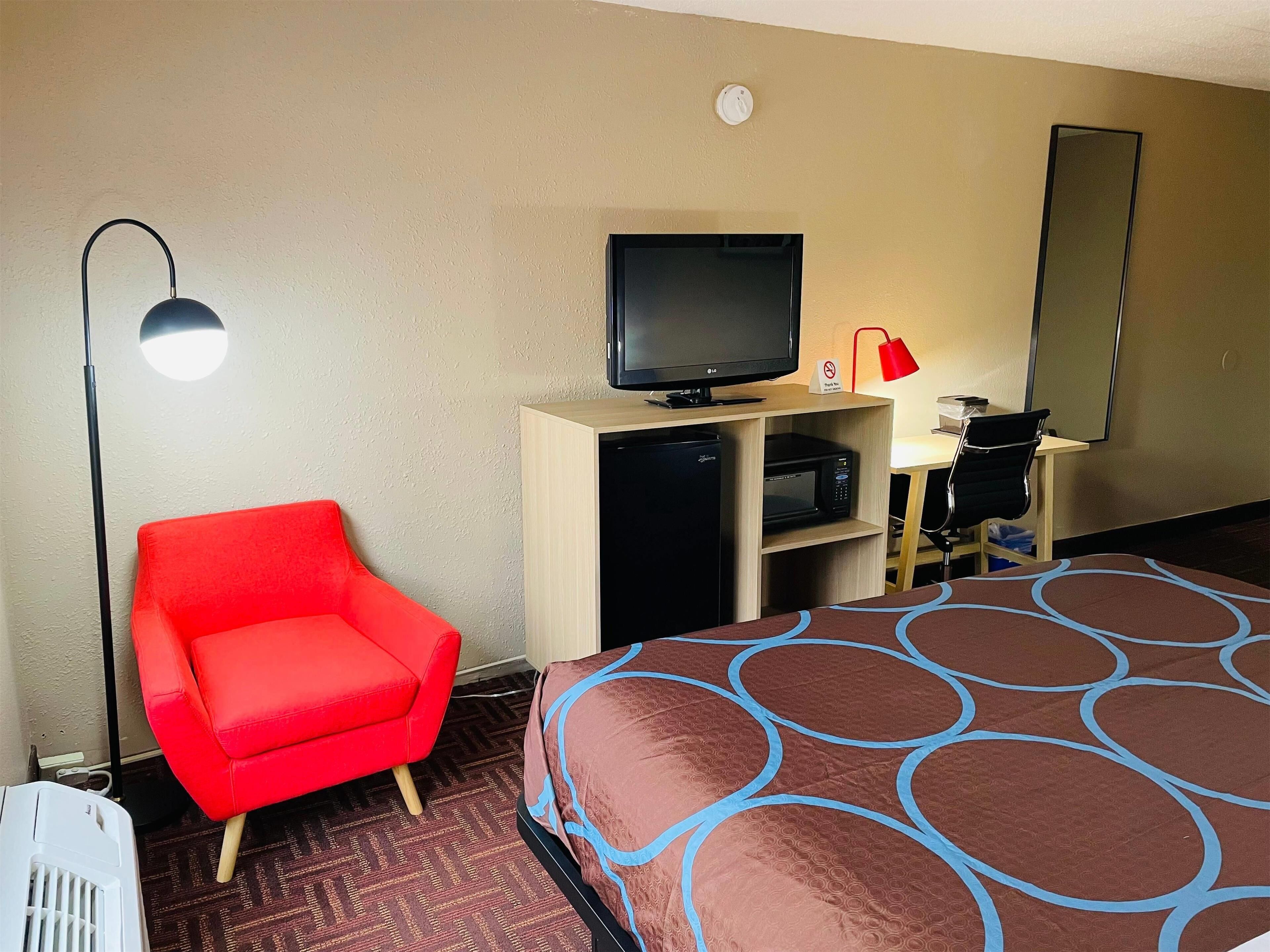 A hotel room with a bed, a red armchair, a desk with a computer, a television, and a microwave.
