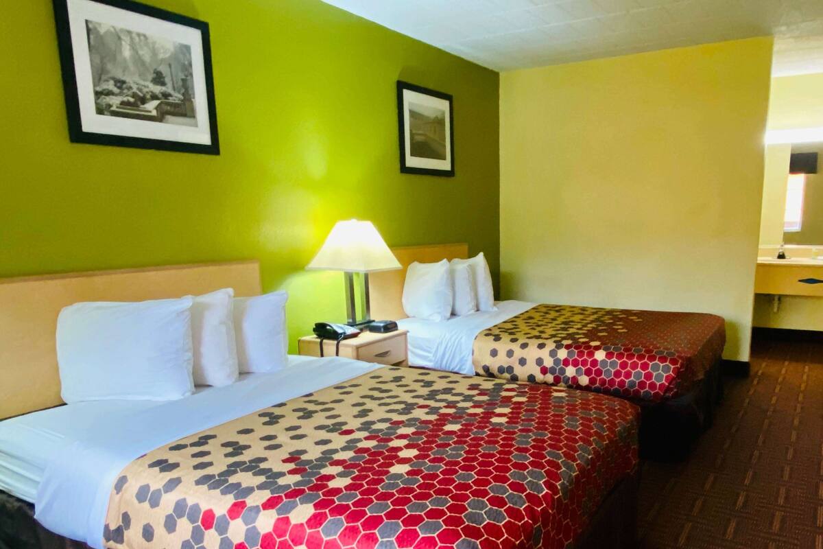 Une chambre d’hôtel avec deux lits, une table de chevet avec une lampe et deux tableaux encadrés au mur.