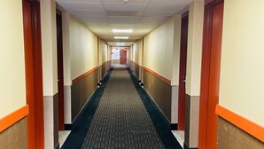 Un long couloir étroit, dont le sol est recouvert de moquette et où l’on trouve des portes en bois de part et d’autre.