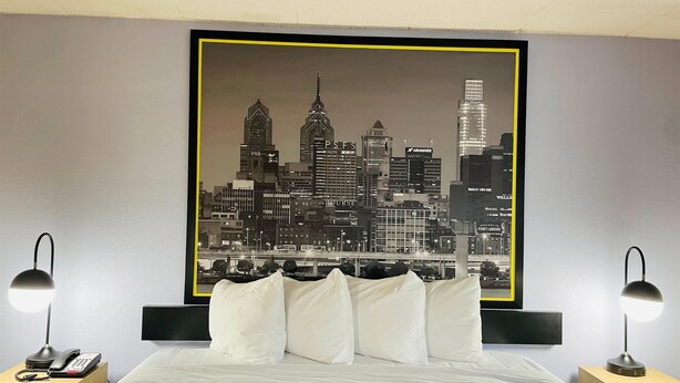 Une chambre d’hôtel avec un lit, deux tables de chevet, une œuvre d’art représentant un paysage urbain accrochée au mur et une couvre-lit à motifs.