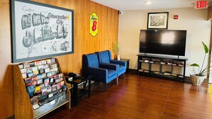 Un hall d’entrée avec une pancarte d’accueil encadrée, le logo de Super 8, un canapé bleu, un téléviseur posé sur un meuble et une petite table avec une plante.