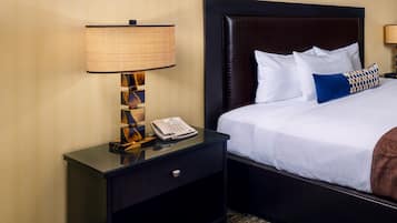 A hotel room with a bed, a nightstand with a lamp, a telephone, and a brown throw blanket.