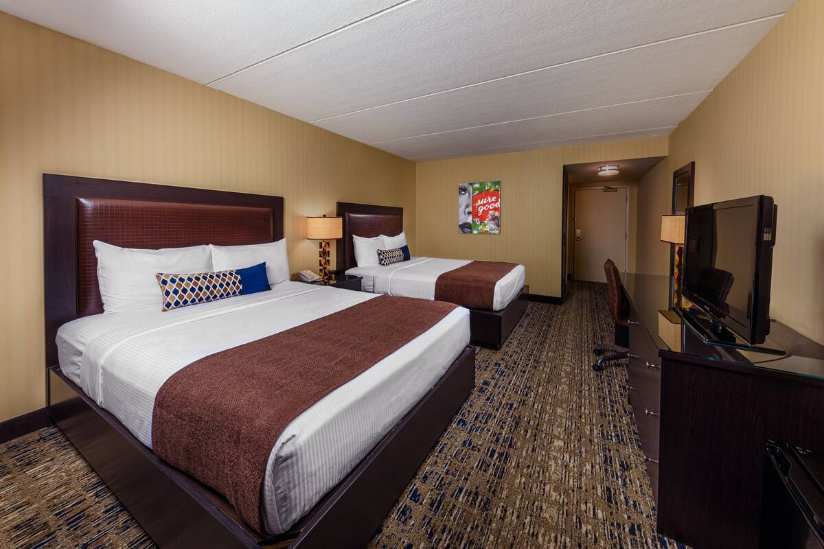 Une chambre d’hôtel avec deux lits, un bureau, une télévision et un sol recouvert de moquette.