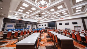 Un salón de conferencias con varias mesas y sillas, ventanas amplias y luminarias modernas.