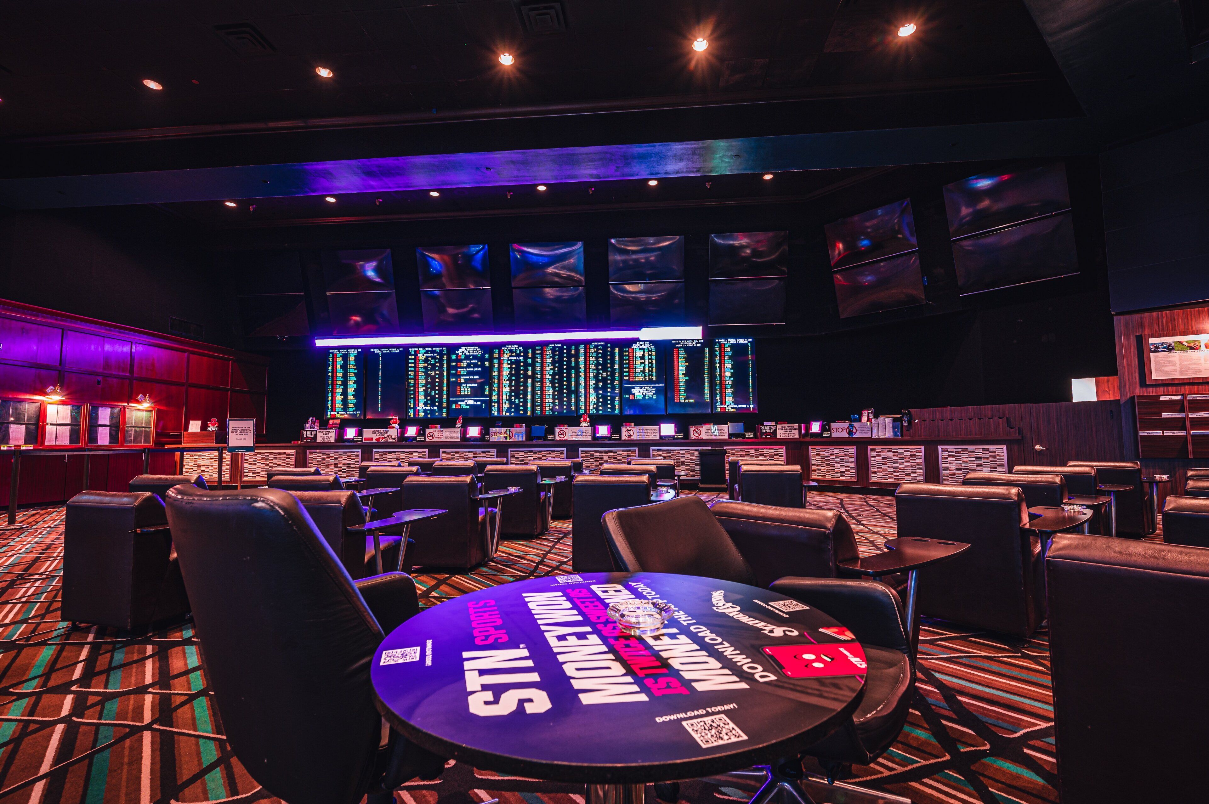 A casino with multiple gaming tables, a bar area, and a large screen displaying information.