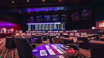 A casino with multiple gaming tables, a bar area, and a large screen displaying information.