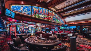 Un casino con un gran letrero colorido que dice "BOULDERSTONE" y múltiples máquinas tragamonedas.