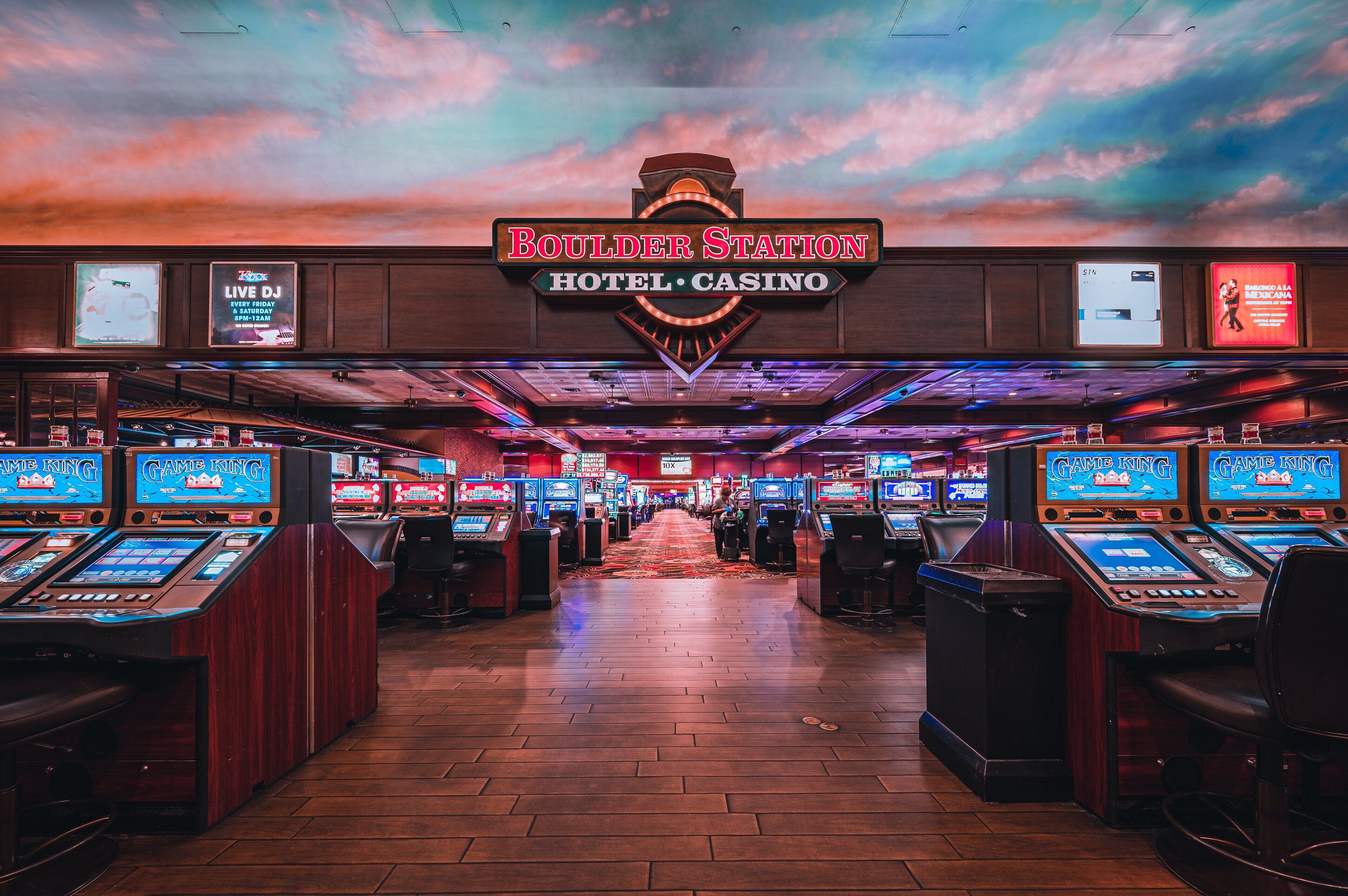 Un casino con múltiples máquinas de juego, un letrero de neón para Boulder Station Hotel & Casino y una alfombra roja que conduce a la entrada.