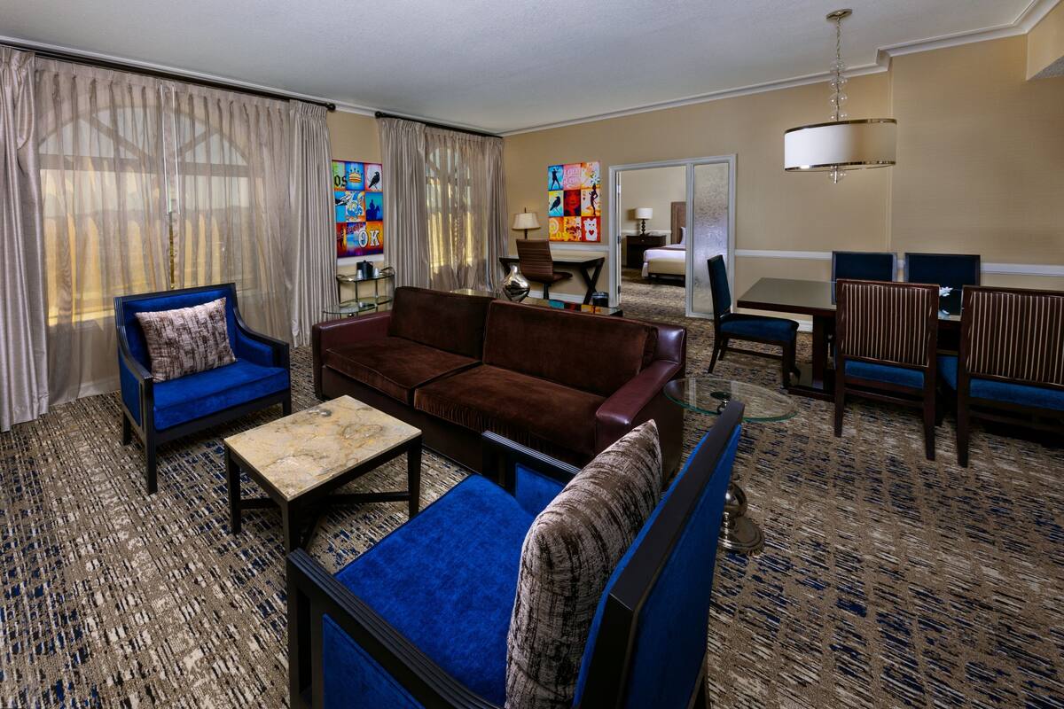 Une chambre d’hôtel dotée d’un espace salon comprenant un canapé, des fauteuils, une table basse et une table à manger avec des chaises.