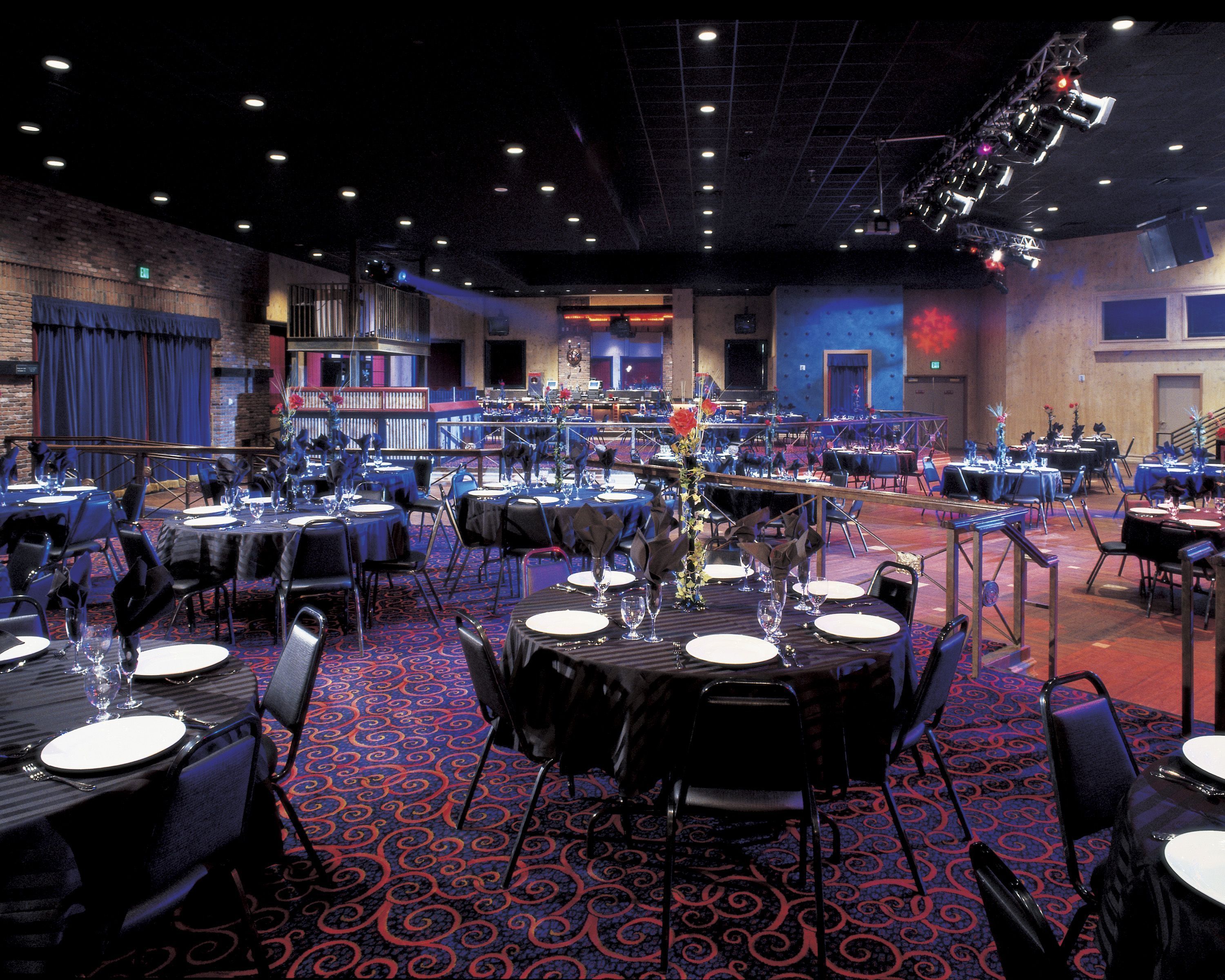 A banquet hall with tables set for dining, a stage with lighting equipment, and a patterned carpet.