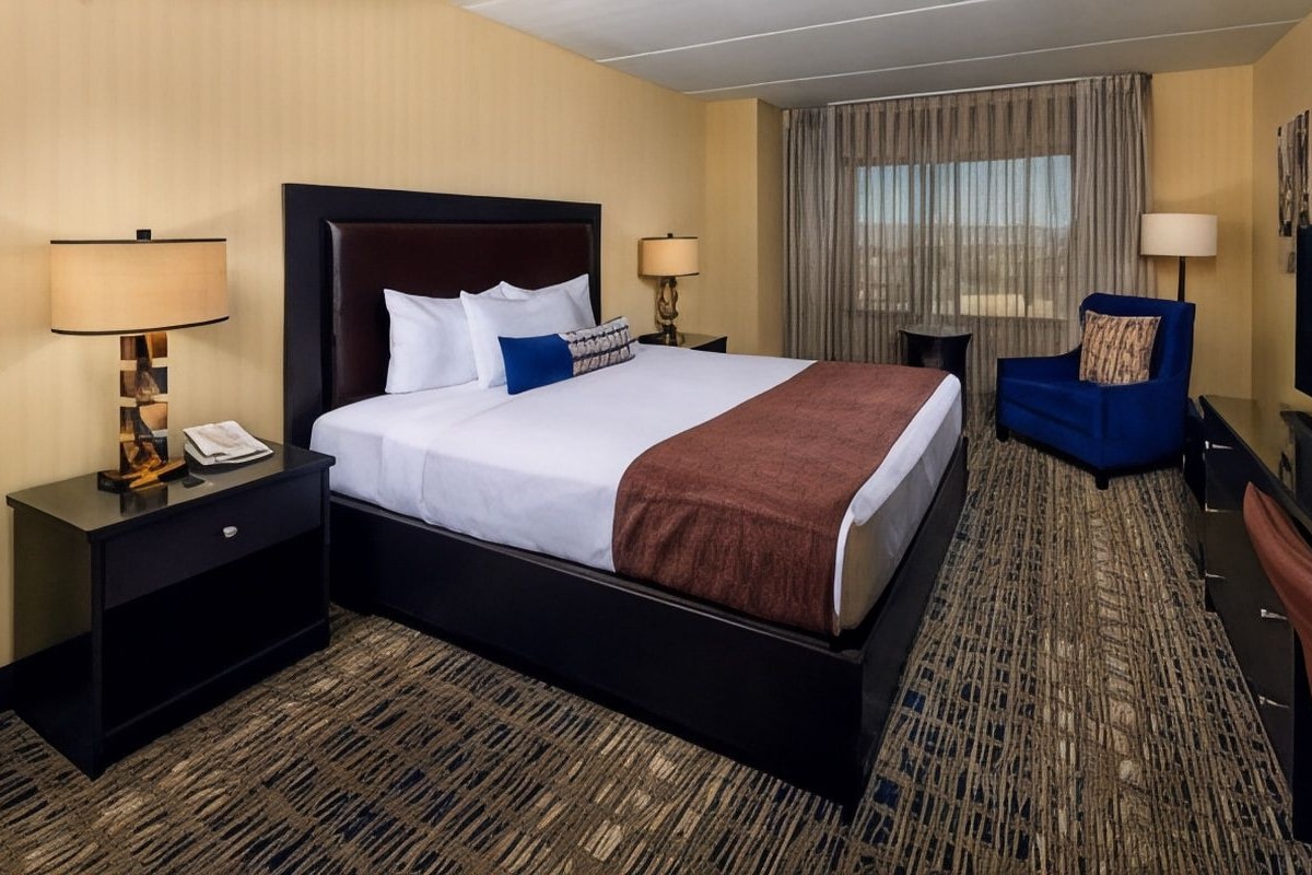 A hotel room with a large bed, a desk, a chair, a television, and a window with curtains.