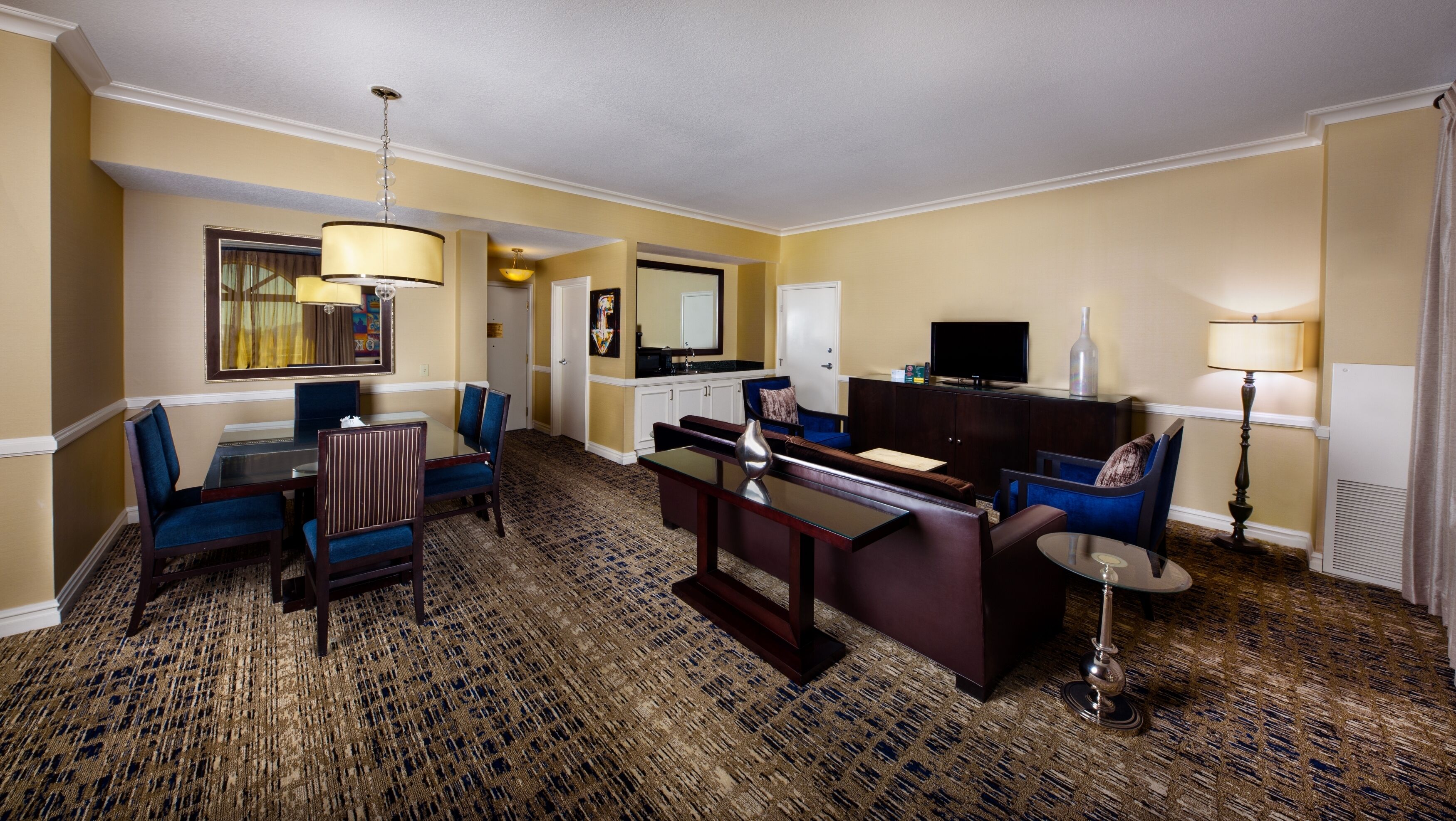 Habitación de hotel con comedor, sofá, televisor y lámpara.
