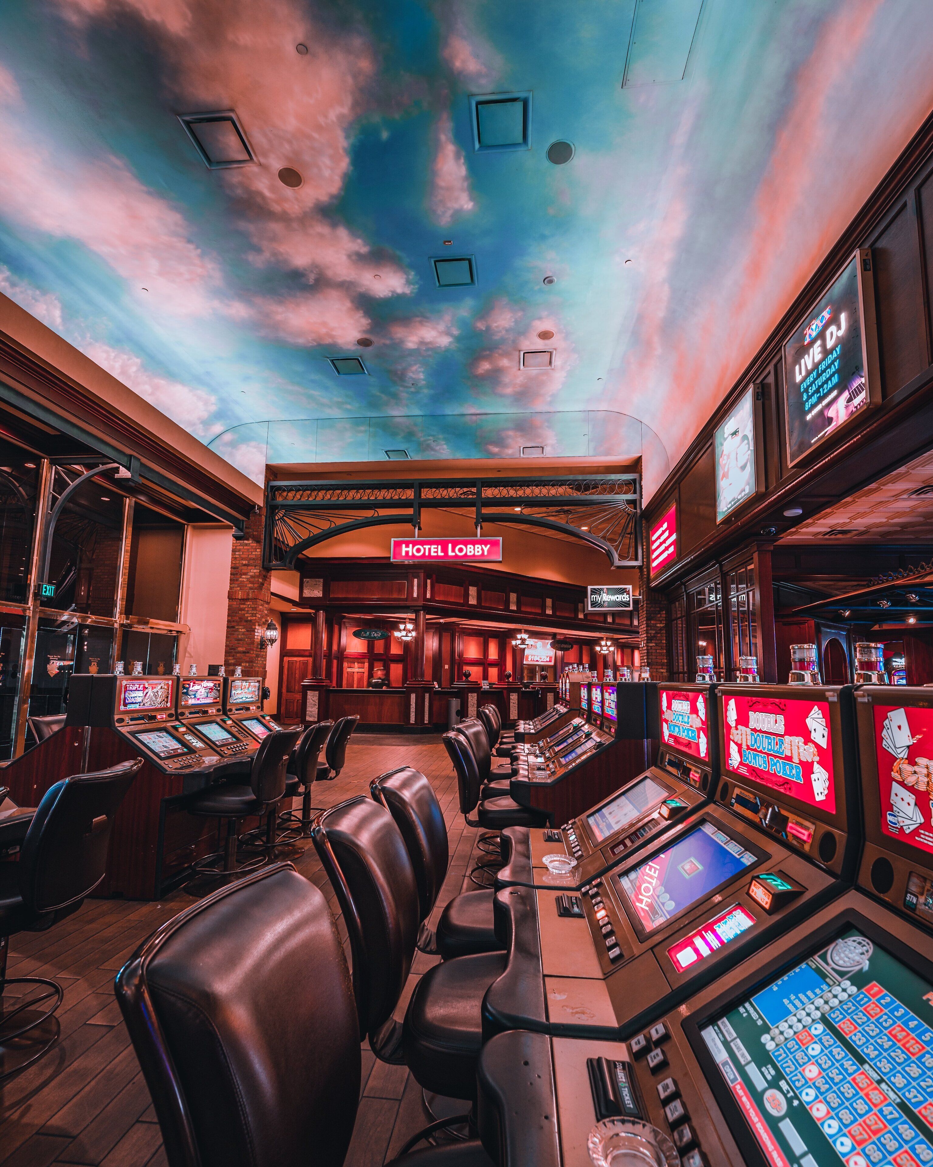 A casino floor with multiple gaming tables and chairs, a hotel lobby sign, and slot machines.