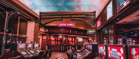 A casino floor with multiple gaming tables and chairs, a hotel lobby sign, and slot machines.