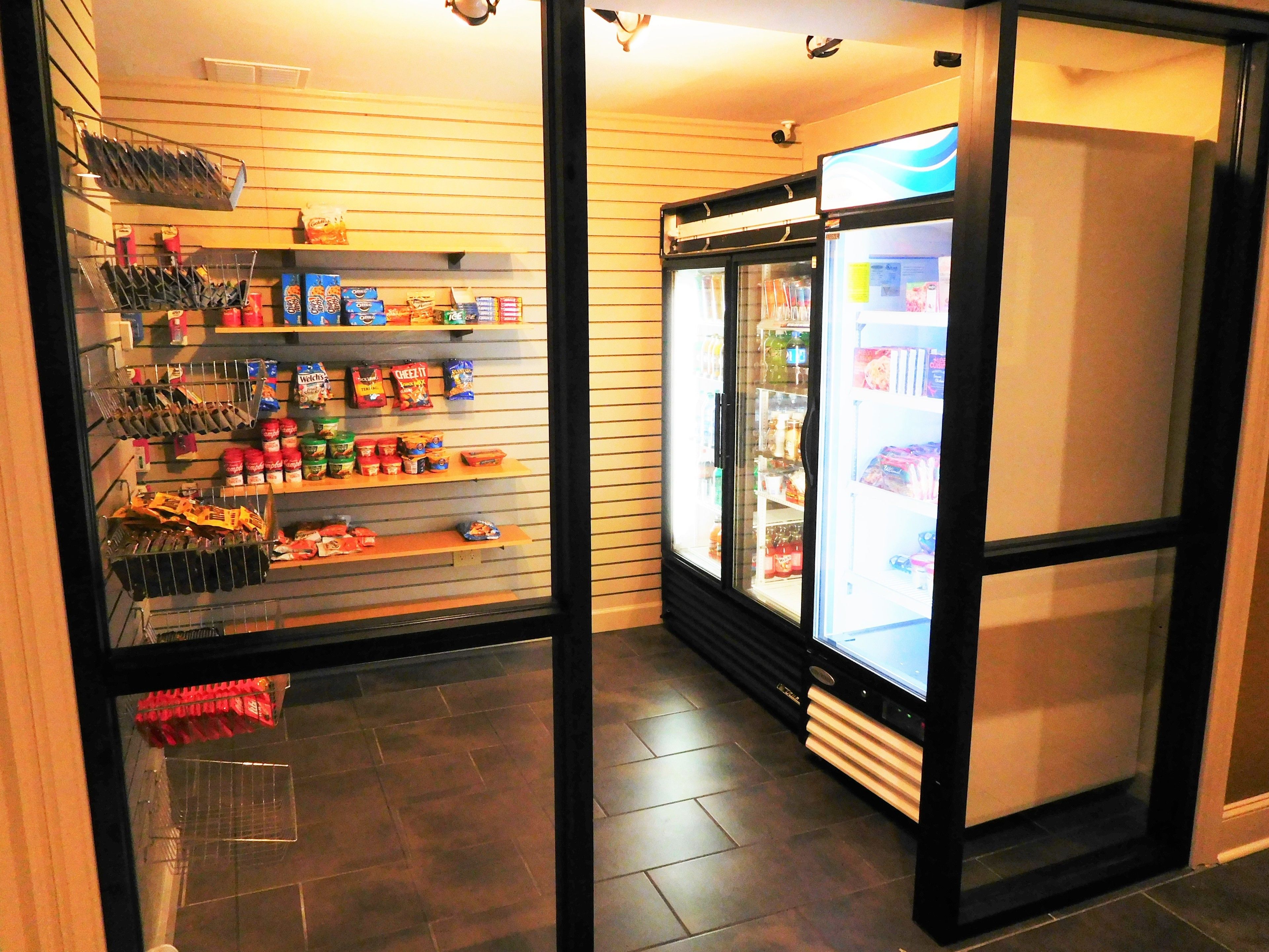 A corner of a store with shelves stocked with snacks and beverages, and a refrigerated display case.