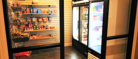 A corner of a store with shelves stocked with snacks and beverages, and a refrigerated display case.