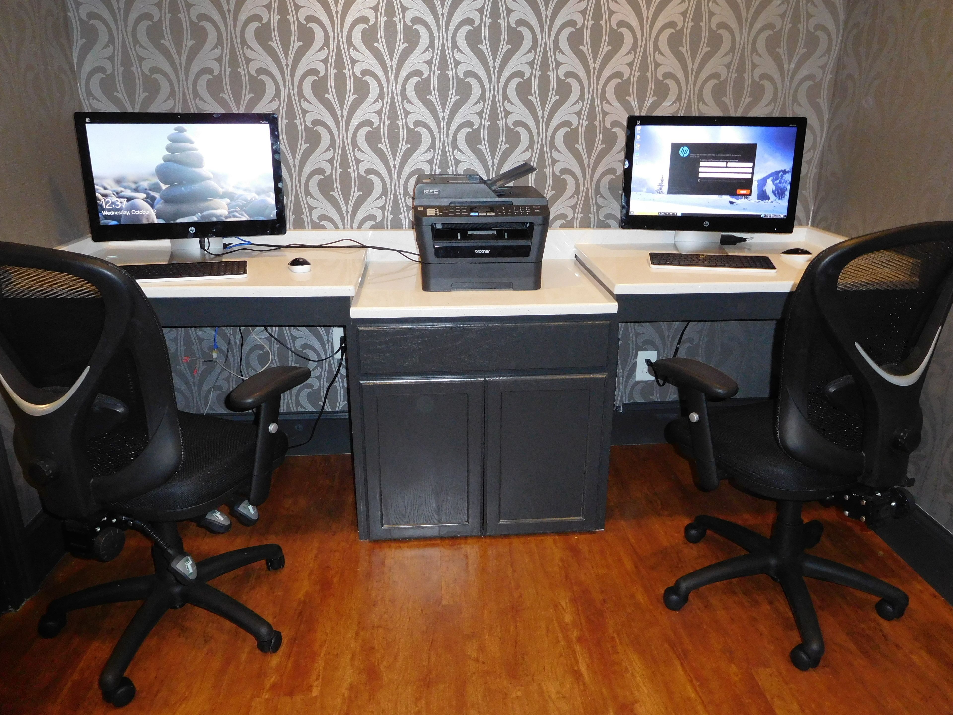 A workspace with two monitors, a printer, and two office chairs.