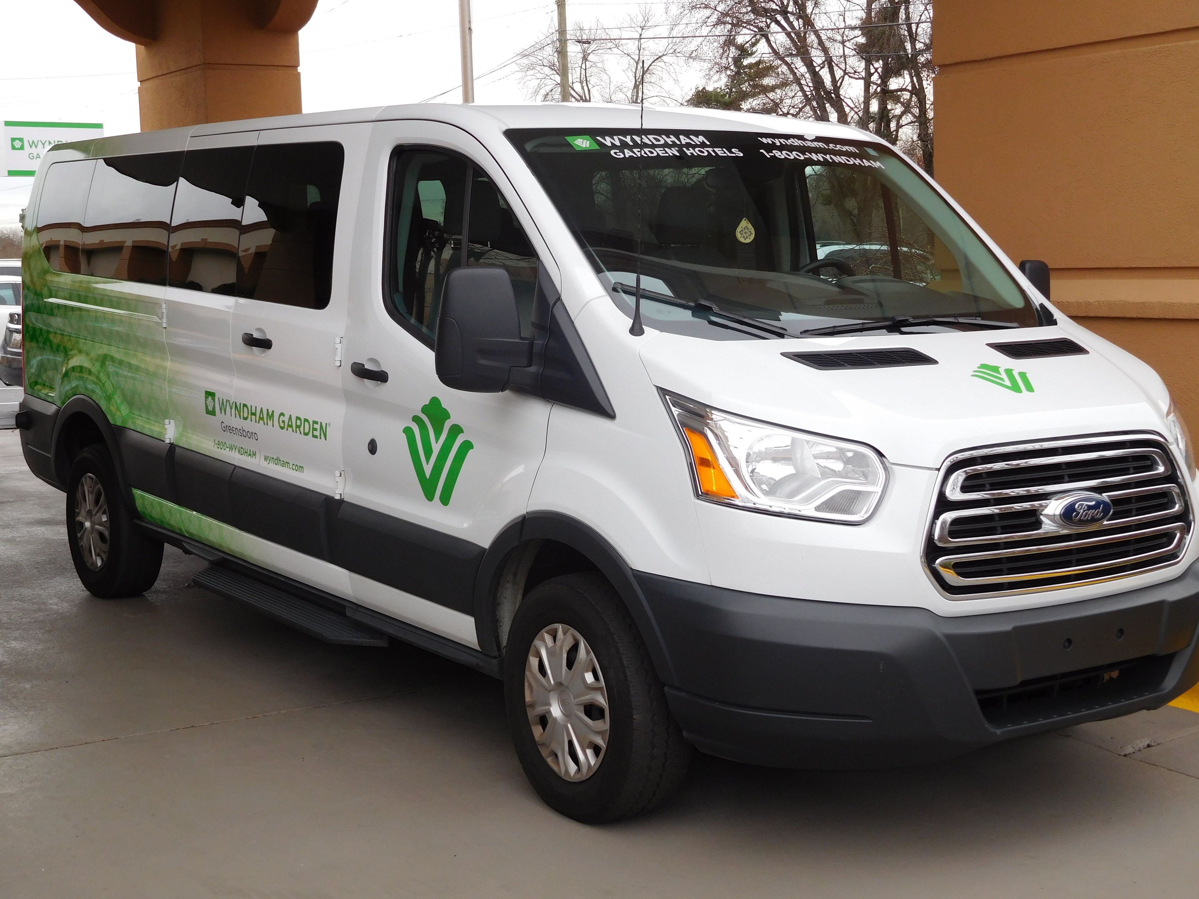 Una camioneta blanca con la marca WYNDHAM GARDEN HOTELS en verde y negro, estacionada en un estacionamiento.