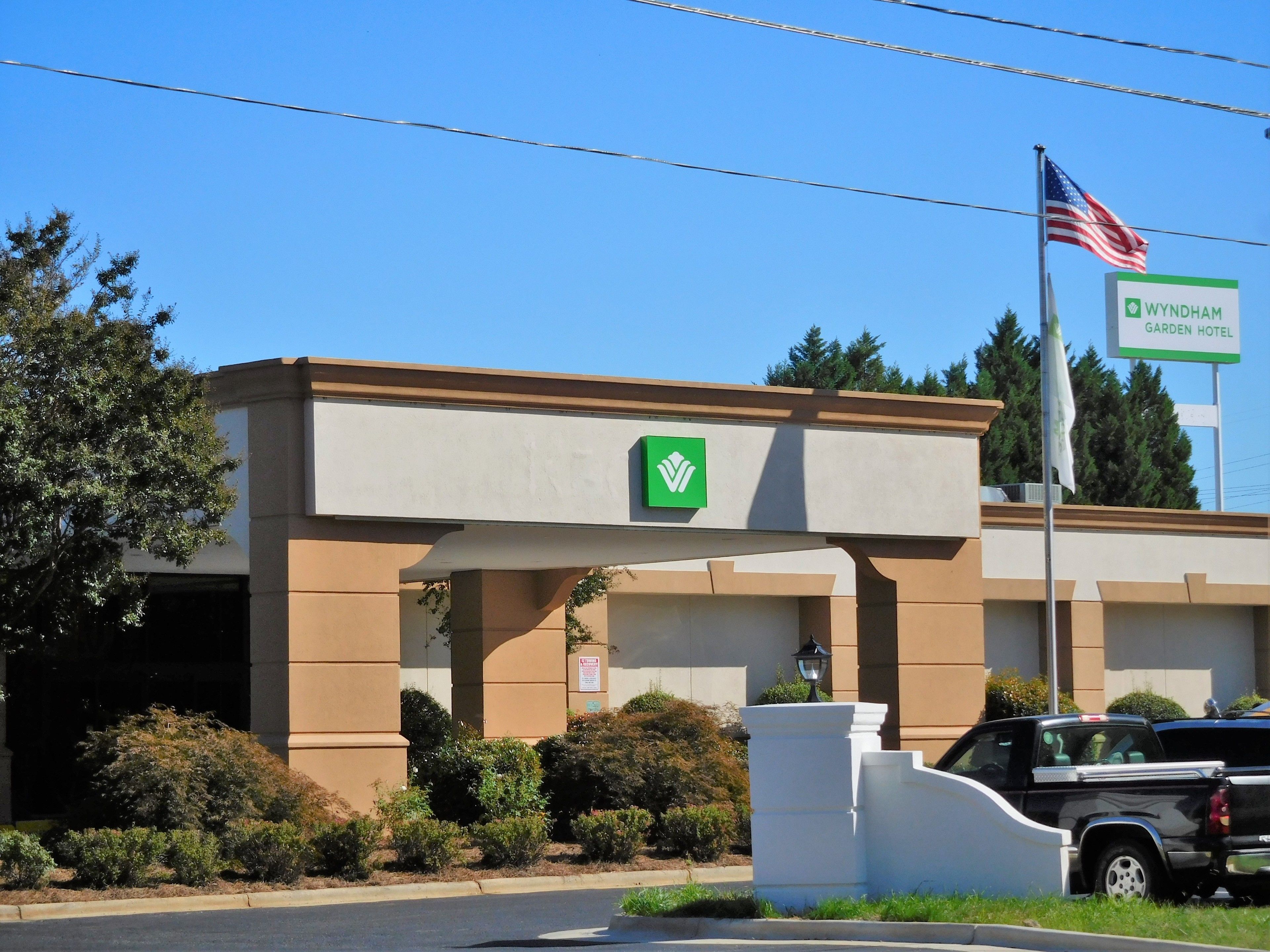 A Wyndham Garden Hotel entrance with a clear sky, an American flag, and a black pickup truck parked in front.