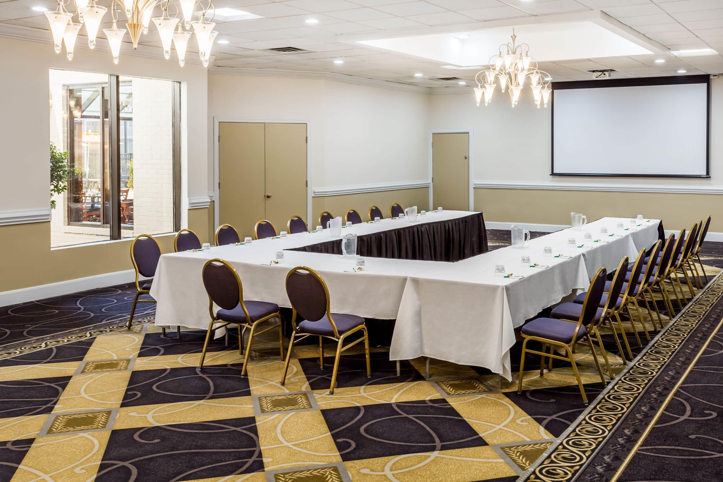 A conference room with a long table, chairs, a projector screen, and a chandelier.