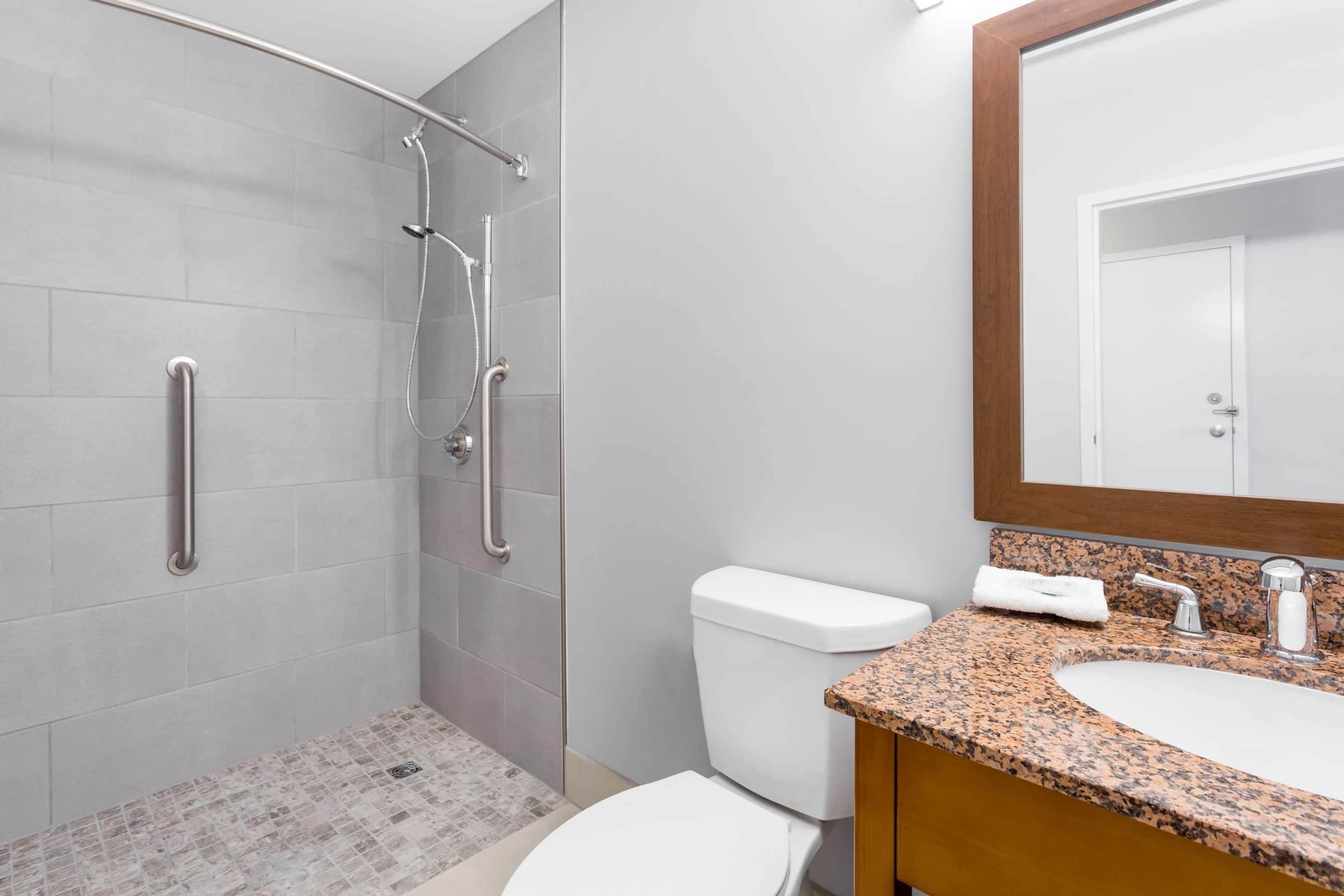 A bathroom with a shower, toilet, sink, and mirror.