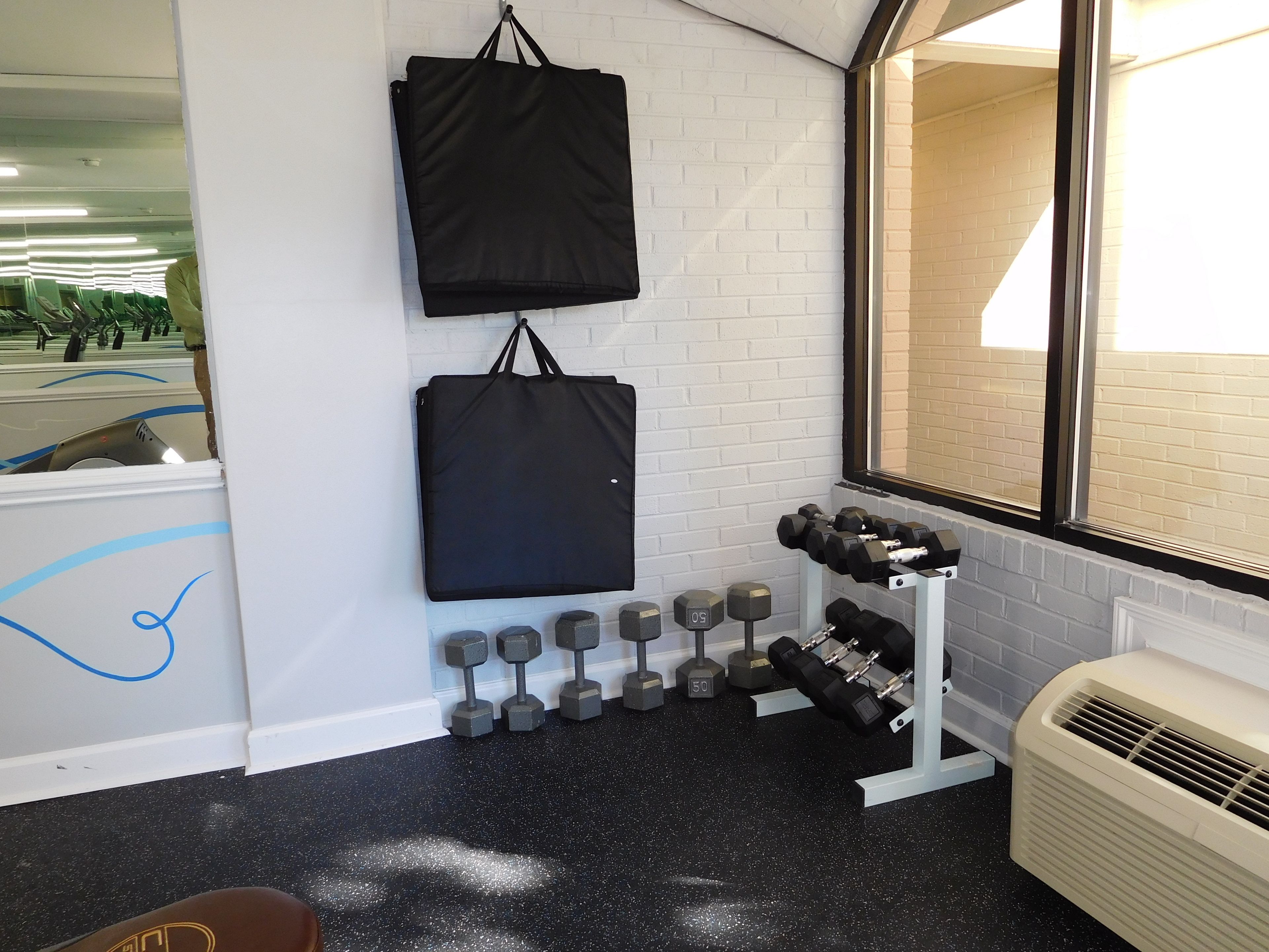 A gym with a mirrored wall, a black mat, a rack of dumbbells, and a white air conditioner.