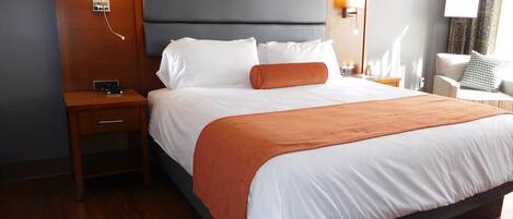 A hotel room with a large bed, wooden headboard, bedside lamps, a nightstand, and a chair.