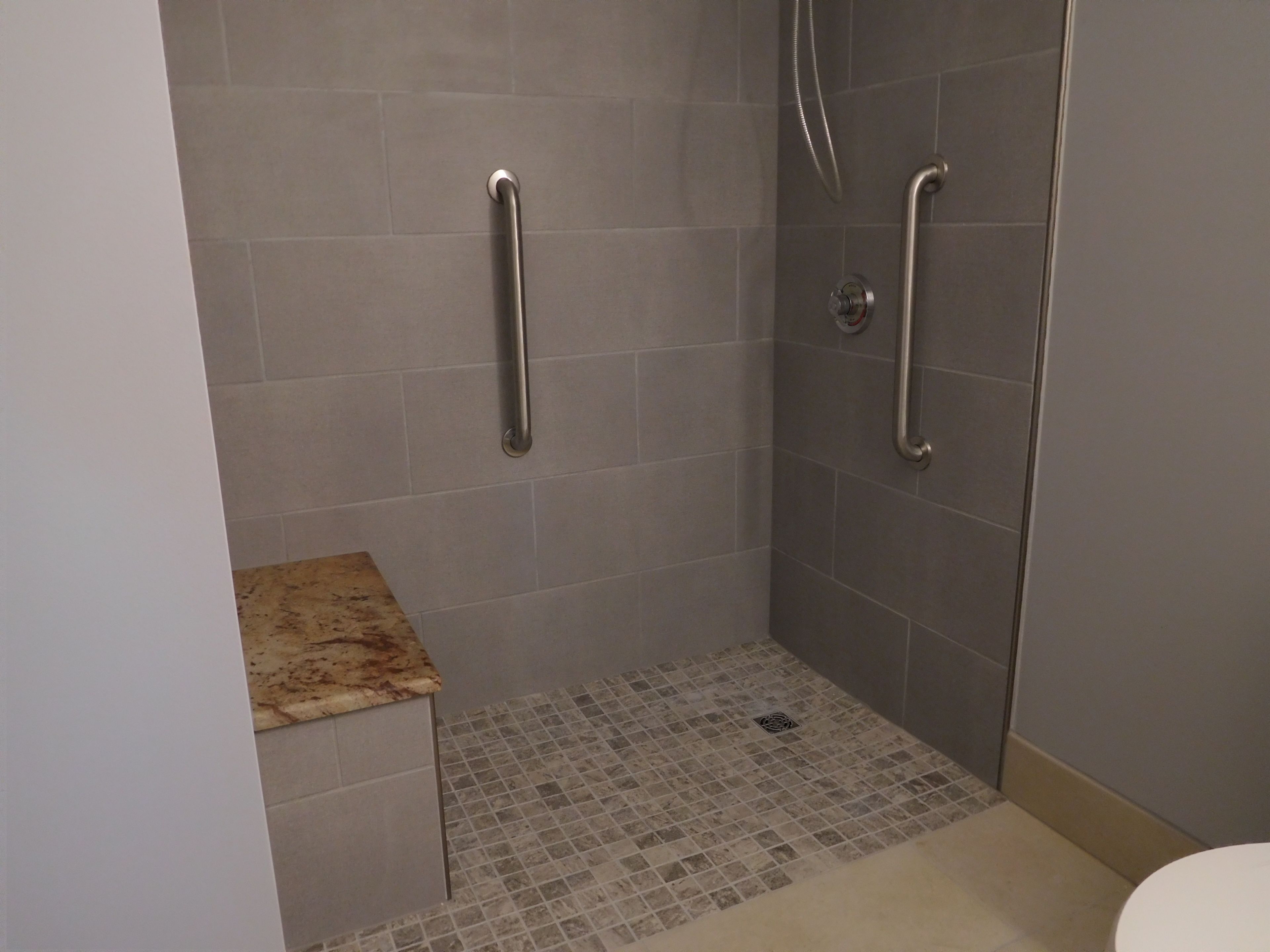 A shower area with grab bars, a tiled floor, and a small countertop.