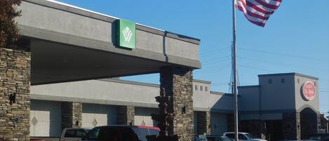 Un edificio con fachada de piedra, un letrero verde con logotipo blanco y una bandera estadounidense.