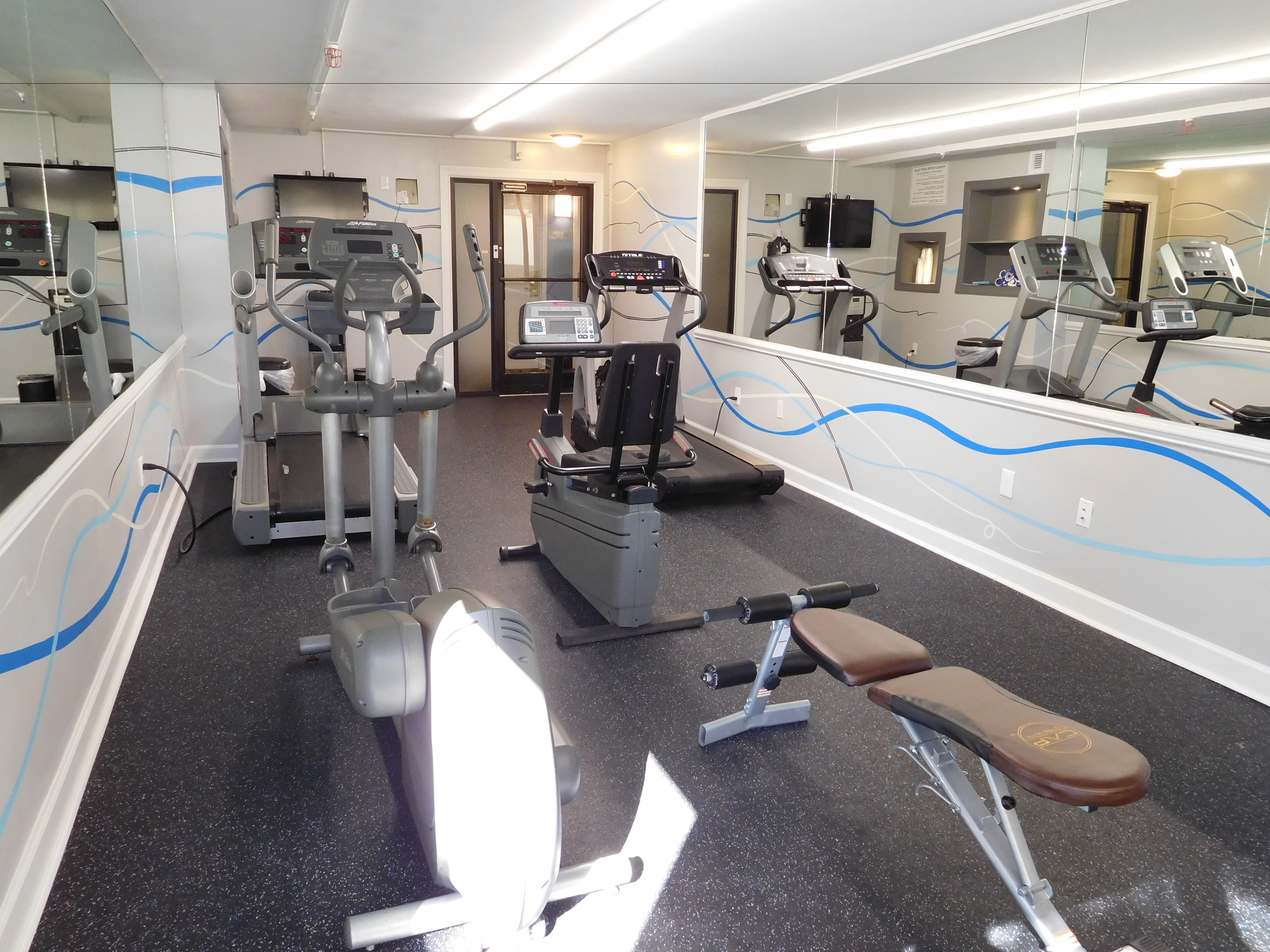 A gym with various exercise machines, a bench, and mirrors on the walls.