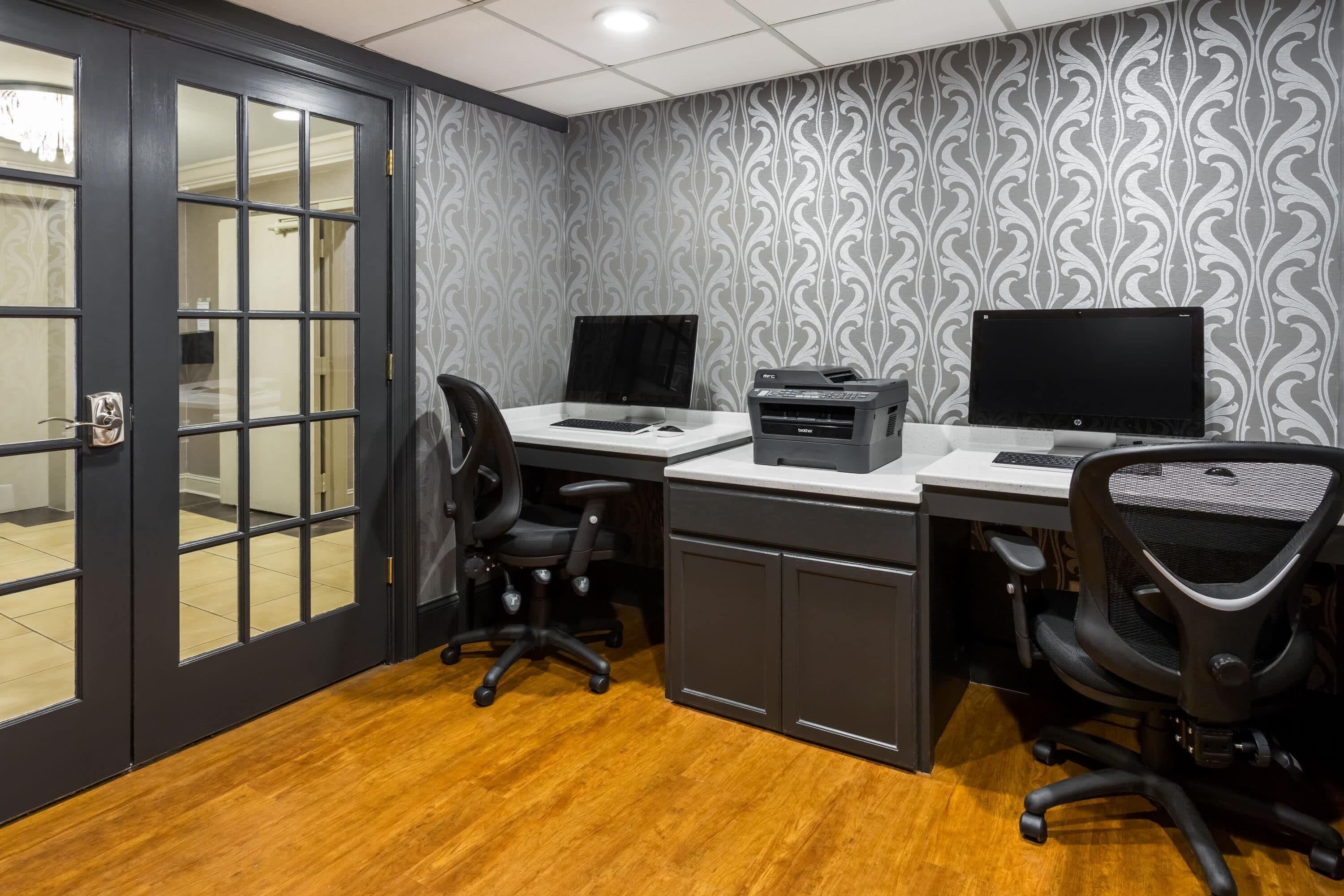 A room with a desk, two monitors, a printer, and two office chairs.