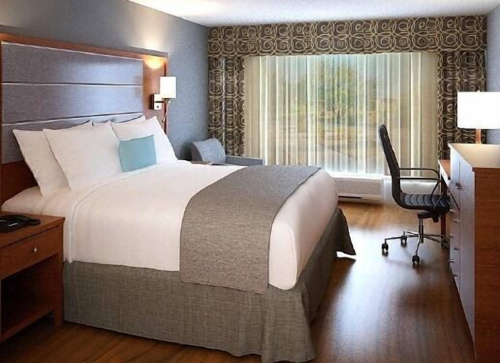 Een hotelkamer met een groot bed, een bureau, een stoel en een raam met gordijnen.