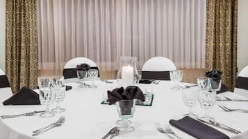 A table set for dining with clear glassware, a candle centerpiece, and a patterned curtain backdrop.
